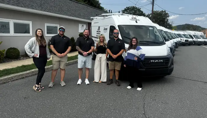 The JB Plumbing HVAC and Construction office team standing in front of the company service fleet